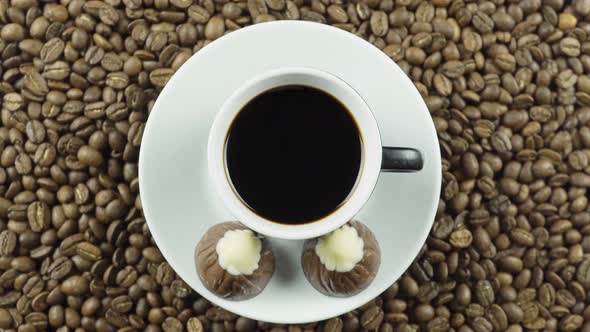Chocolate Candy And A Cup Of Black Coffee On A Background Of Rotating Coffee Beans.