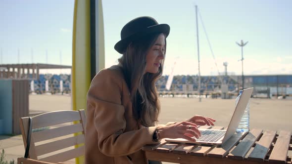 Young Brunette Woman Is Chatting Online By Laptop with Wifi Sitting on Street alt