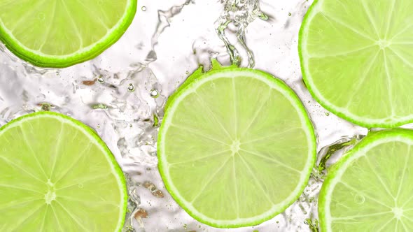 Super Slow Motion Shot of Splashing Fresh Lime Slices Into Water on White Background at 1000 Fps alt