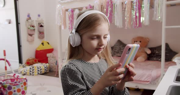 The 7Yearold Girl in the Children's Room with Headphones and Using Smartphone alt