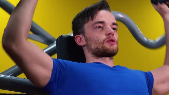 A Young Fit Man Trains on a Machine in a Gym, Closeup From Below alt