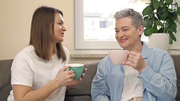 Cheerful Women of Different Ages Drink Tea or Coffee While Sitting on the Sofa in the Living Room