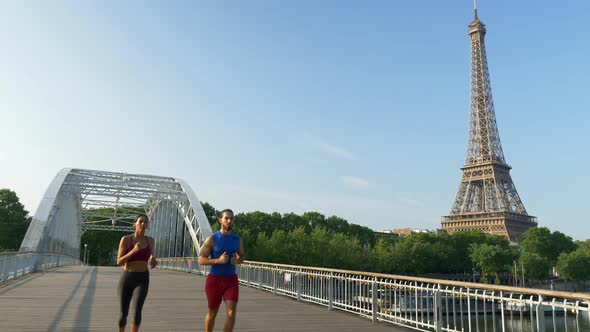 A man woman couple running across a bridge with the Eiffel Tower alt