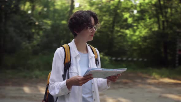 Tourist View Of The Road In The Forest, Travel Lifestyle. A Girl With A Backpack Holds A Map. Woman alt