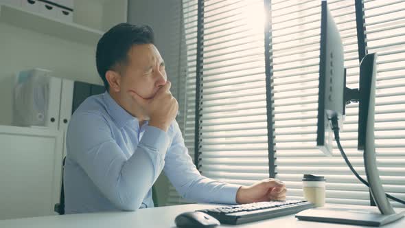 Exhausted Asain business man using laptop computer working in office. alt