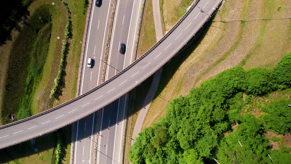 Aerial top down view of vehicles running on highway and crossing under overpass on bright sunny day. alt
