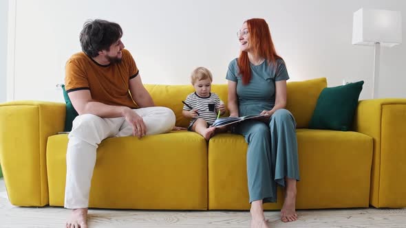 Family Sitting on Yellow Couch and Reading Book Together  the Baby Holding a Pen and Lily alt