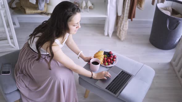 Lady Works on Laptop at Soft Pouf with Coffee and Croissant