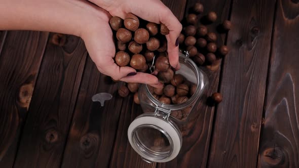 Closeup of a Woman Pouring a Macadamia Nut Into a Jar on a Wooden Background alt