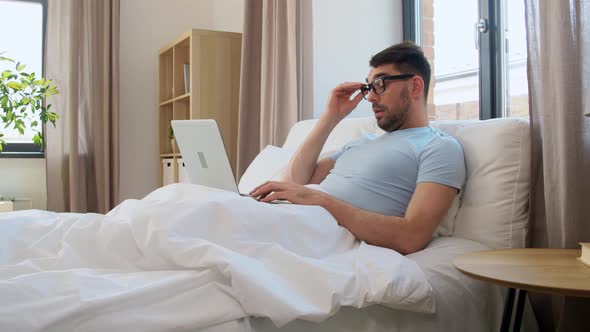 Tired Man in Glasses with Laptop Working in Bed