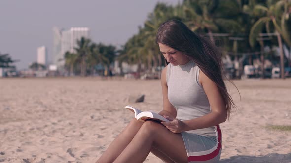 Tremendous Girl in Light Dress Reads Book Sitting on Sand alt