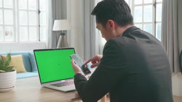Asian Businessman With Green Screen Computer Using Mobile Phone While Working At Home alt