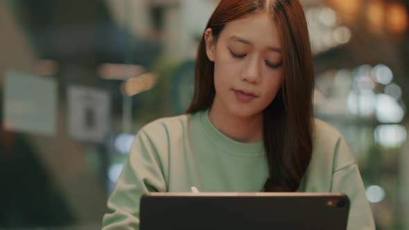 Young asian female freelance using digital tablet working, drawing freelance work sit in coffee shop