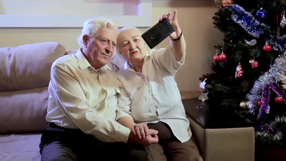 An elderly couple takes a selfie near the Christmas tree at home for Christmas