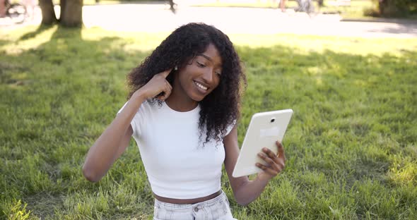 Joyful Black Woman Listening to Music on Tablet in Park in Sunny Day alt
