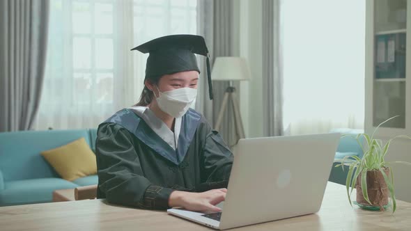 Asian Woman Wear Protection Mask And Wear A Graduation Gown And Cap Use Laptop Computer alt