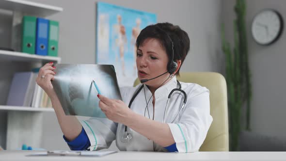 Female Doctor in Medical Coat and Headset Making Conference Call on Laptop Computer
