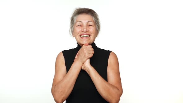 Elder Wrinkled Woman with White Tied Hair Looking at Camera with Beautiful Smile Clenching Her Hands alt