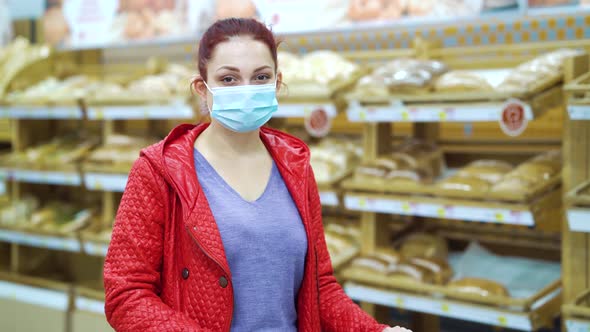 Woman in mask standing in bakery against shelves with bread alt