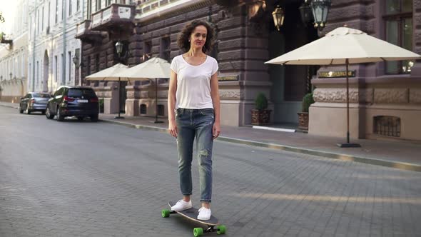 Attractive Brunette Woman in White Tshirt Blue Jeans and White Sneakers Skateboarding at Sunrise in alt