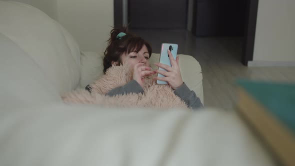 Woman Lies on the Sofa and Uses the Phone Instead of a Book To Read