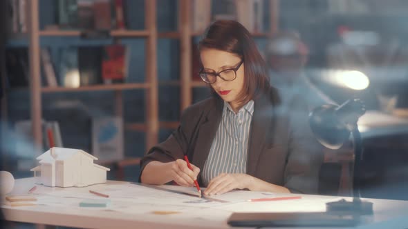 Thoughtful Female Architect Working on Floor Plan at Desk in Office alt