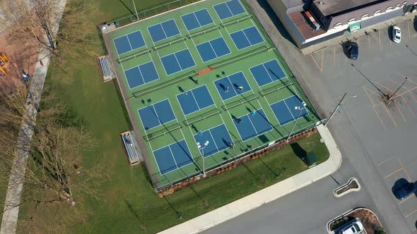 Birds Eye View of Tennis Players in a City Park, Drone Truck Left past the Sports Courts alt