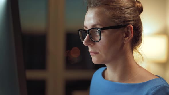 Woman in Glasses Looking on the Monitor and Surfing Internet. The Monitor Screen Is Reflected in the alt