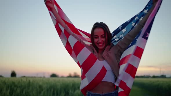 Cheerful Young Woman Wrapped in United States Flag Outdoors with Polica Lights on Face alt