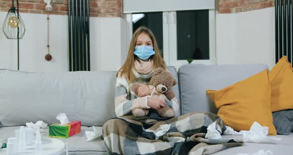 Teen Girl in Medical Mask in Living-Room on Home Self Isolation During Disease, Sickness alt