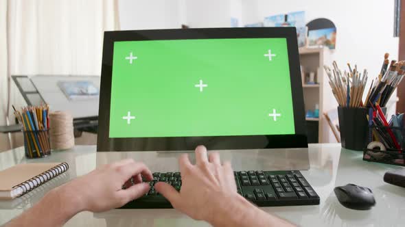 View on Male Hands Working on a Computer with Green Screen on a Glass Table alt