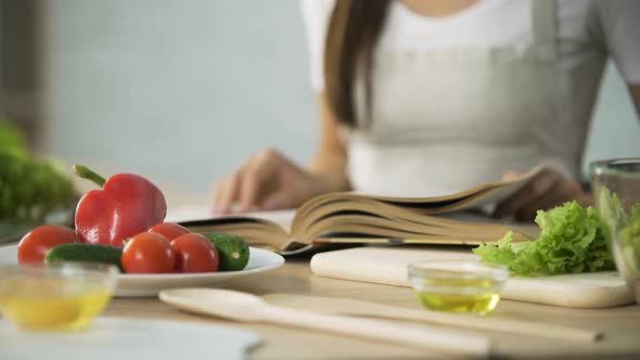 Close-Up of Girl Flipping Through Cooking Book Pages, Choosing Salad Recipe alt