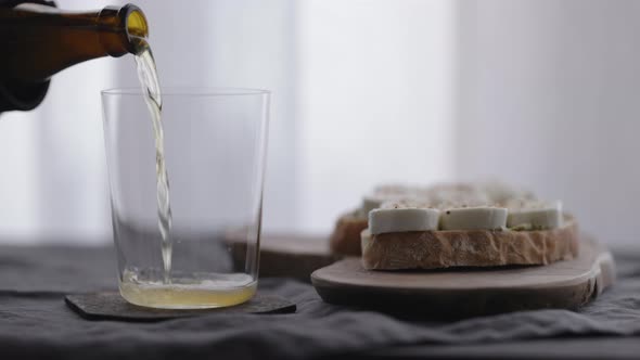 Slow Motion Pour Wheat Beer in a Tumbler Glass Next to Ciabatta Sandwiches with Mozzarella and Pesto alt