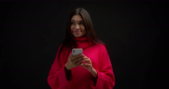 Asian Woman Reads a Nice Message on Her Phone and Smiles on a Black Background