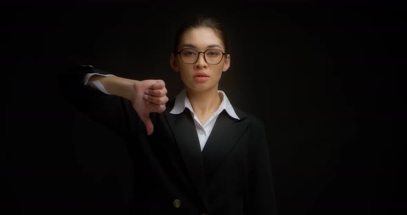 Serious Asian Woman in Business Clothes and Glasses Gives a Thumbs Down
