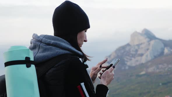 Woman with Backpack Using Smartphone to Find the Right Path on the Top of Mountain alt