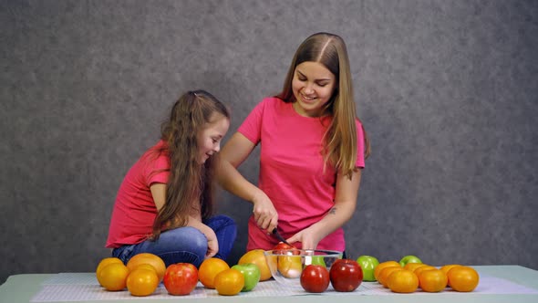 Woman cutting fruits on table. Young woman with daughter preparing healthy food alt