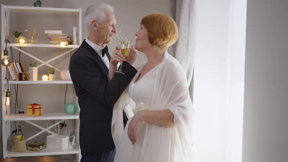 Smiling Senior Groom and Bride Drinking Bruderschaft Champagne Standing Indoors alt