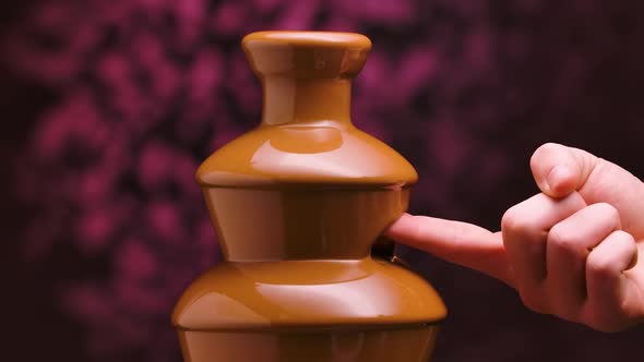 Melted Milk Chocolate Flows in a Chocolate Fountain on Blurry Purple Background alt