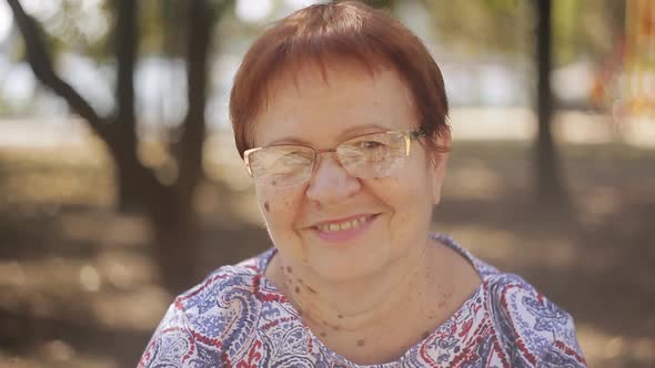 Portrait of Happy Elderly Woman in Park Laughing Enjoying Retired Lifestyle Wearing Glasses