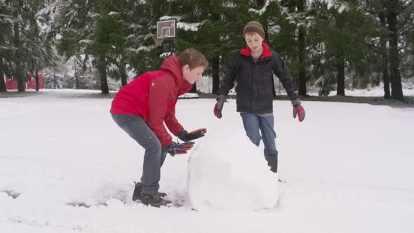 Two boys rolling a snow ball in winter