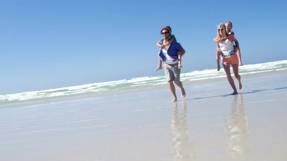 Parents giving piggyback ride to their children while running on shore at beach alt