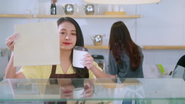 Attractive asian female cafe worker  giving takeaway food bag to customer alt