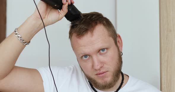 Handsome man in white t-shirts cutting hair personally himself with machine trimmer, clipper at home alt