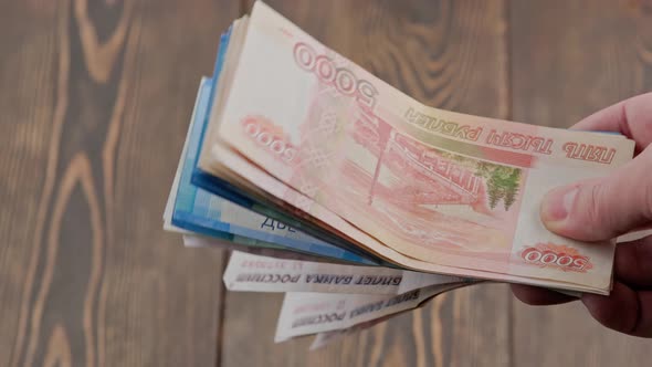 Caucasian Hand Shaking Small Stack of Russian Ruble Banknotes Over Wooden Background