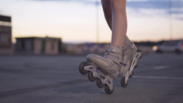 Slim Female Legs in Roller Skates Riding at Dusk on Empty Parking Lot. Unrecognizable Young alt