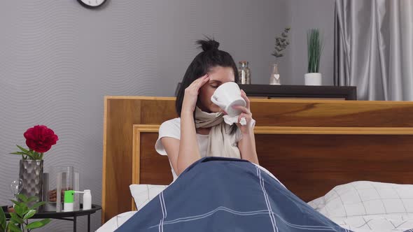 Upset Sick Young Woman which Sitting in Bedroom Bed and Drinking Tea while is Treated at Home alt