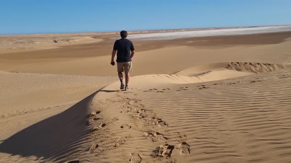 Man walking in the Sahara desert and leaving footprints. alt