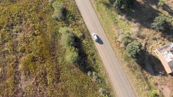 aerial following a silver car travelling on an open road with fields on both sides alt