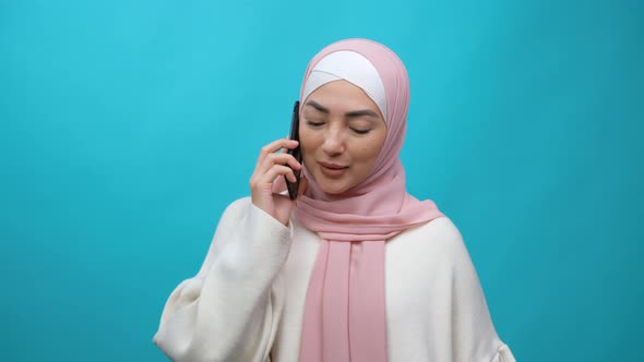 Smiling Young Muslim Woman in Hijab Using Speaking Talking on Mobile Cell Phone Conducting Pleasant